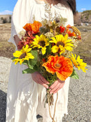 Dried natural poppies and sunflowers bouquet held in hands with rustic outdoor background, wholesale bulk arrangement.