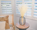Bulk dried white Gypsophila baby’s breath arranged in a gray vase on a wooden side table.