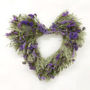 A heart-shaped wreath made of green and purple dried flowers and oats.