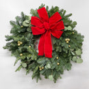 Natural dried holiday wreath with pine branches, eucalyptus leaves, gold berries, and large red velvet bow, wholesale bulk.