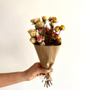 Hand holding natural dried spray rose bouquet in yellow, pink, and white wrapped in brown paper.