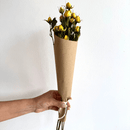 Hand holding bulk natural yellow dried spray rose bunch wrapped in brown kraft paper.