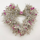 A heart-shaped wreath made of dried flowers, primarily in shades of pink and white, with a beige base.