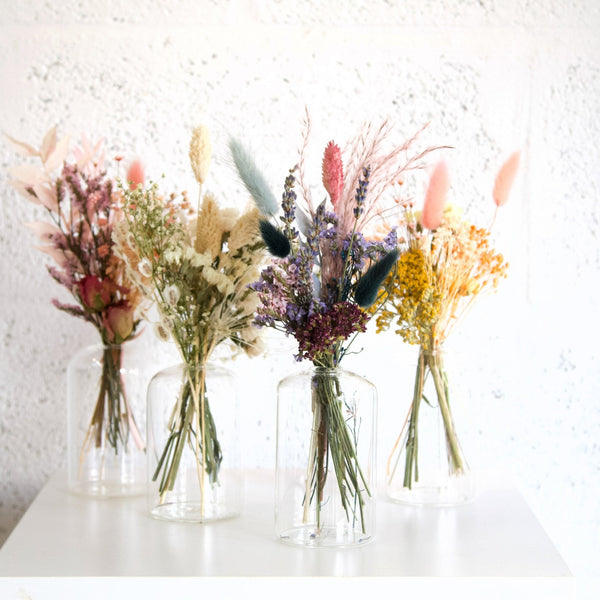 Four glass vases with dried floral arrangements on a white surface.