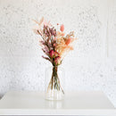 Clear glass vase with pink and orange flowers on a white surface against a textured white wall.