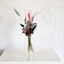 Natural dried flower bud bouquet in clear glass vase with purple, beige, and green tones.