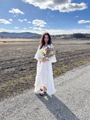 Woman in white dress holding a dried dogwood and daffodils bouquet outdoors under blue sky.