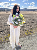 Woman in white dress holding large natural dried hydrangeas and daisies bouquet outdoors bulk wholesale.
