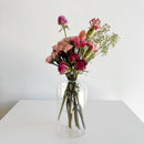 Clear glass vase with pink and red flowers on a white surface and background