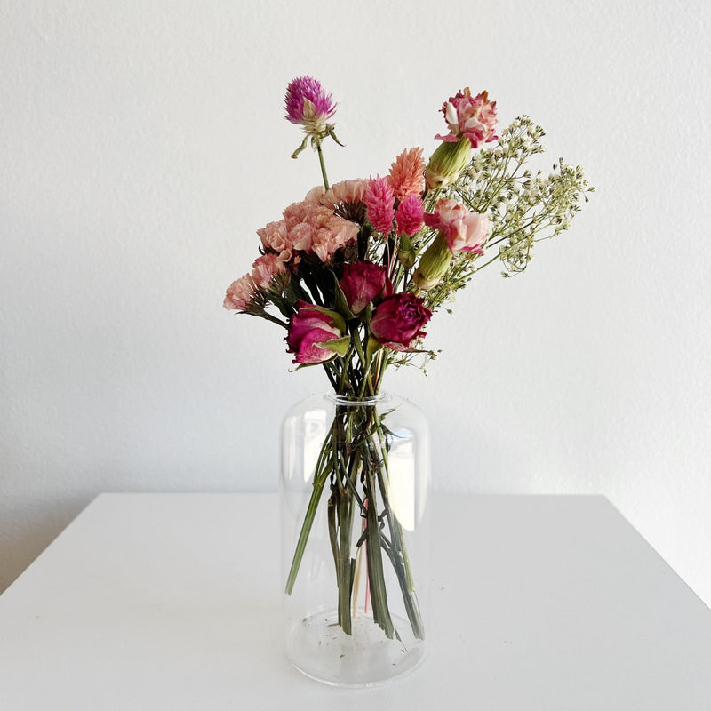 Clear glass vase with pink and red flowers on a white surface and background