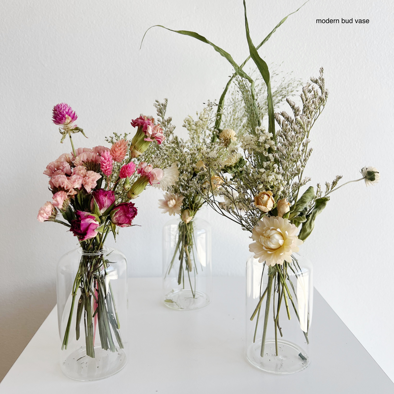 Three glass vases with floral arrangements on a white surface.