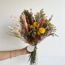 Bouquet of dried flowers held by a hand with a plain background