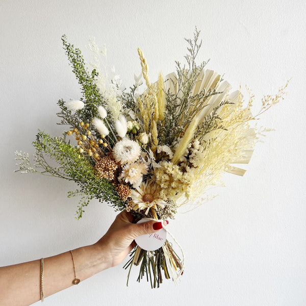 Bouquet of dried flowers held by a hand against a white background