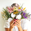 Brightly colored natural dried flower bundles in pink, yellow, purple, and white held in bulk for wholesale use.