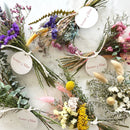 Small dried flower bundles in purple, lavender, blue, yellow, and pink tones with natural greenery, arranged for wholesale.
