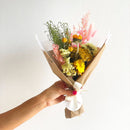 Hand holding a bouquet of flowers wrapped in brown paper against a white background