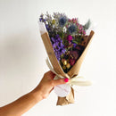 Bouquet of flowers wrapped in brown paper held by a hand against a white background