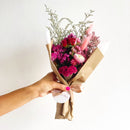 Bouquet of flowers wrapped in brown paper held by a hand on a white background