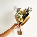 Bouquet of flowers wrapped in brown paper with a white ribbon held by a hand against a light background