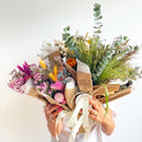 Handheld natural dried flower bouquets in bright, peachy, and green tones wrapped in brown paper for wholesale bulk sale.