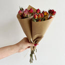Bouquet of red and yellow roses wrapped in brown paper held by a hand against a white background