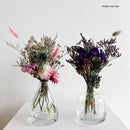 Two clear glass bud vases with dried flowers on a white surface.
