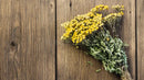 Bulk dried natural yellow tansy flowers tied in a rustic brown twine on wooden surface.
