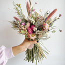 Bouquet of dried flowers held by a person against a plain background