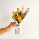 Small dried flower bundle with bright orange and yellow blooms, pink accents, and green stems wrapped in white paper for.