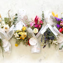 Large dried flower bundles in white, nude, pink, purple, and green tones wrapped in white tissue, natural wholesale bulk.