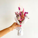 Hand holding pink large dried flower bundle wrapped in white paper, natural wholesale bulk bouquet.