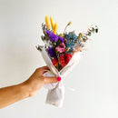 Handheld large bundle of dried flowers in purple, lavender, blue, and yellow tied with white fabric perfect for wholesale.