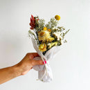 Handheld bundle of natural dried orange and yellow flowers wrapped in white paper for wholesale bulk use.