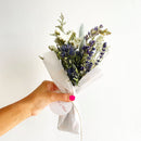 Handheld purple and blue dried flower bundle wrapped in white paper, natural wholesale bulk bouquet.