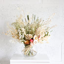 Medium dried flower arrangement with natural beige, white, and soft green tones in clear glass vase.