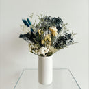 Dried natural flower arrangement with black berries, white blooms, yellow accents, and blue thistles in white cylinder vase.