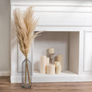 Tall natural dried pampas grass stems in bulk arranged in a glass vase by a white mantel with candles.