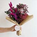 Bouquet of flowers wrapped in brown paper with a visible brand tag on a light background