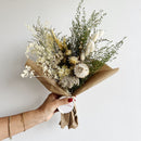 Bouquet of dried flowers held by a hand with a plain background