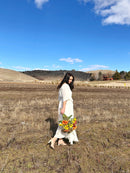 Woman in white dress holding vibrant dried poppies and sunflowers bouquet in natural bulk field setting.