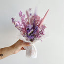 Bouquet of pink and purple flowers held by a hand against a white background