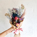 Handheld dried flower bouquet wrap with purple, pink, and beige blooms tied with pink ribbon, natural wholesale bulk.