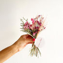 Hand holding small bulk bundle of natural pink dried flowers with greenery and label.