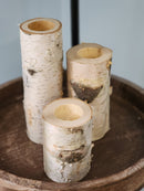 A set of white birch pillar holders of varying heights displayed on a wooden surface.