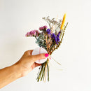 Hand holding a small bouquet of dried flowers against a plain background