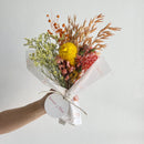 Bouquet of flowers wrapped in white paper held by a person against a light background