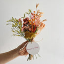 Bouquet of dried flowers held by a hand with 'house of lilac' tag on a light background