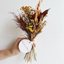 Bouquet of dried flowers held by a hand with a white label on a light background