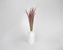 Bulk dried ruby red silk grass bunches with slender red and green stems in white ceramic vase.