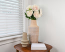 Blush dried peony spray with 12 stems in a textured natural vase on wooden table with books and decor.